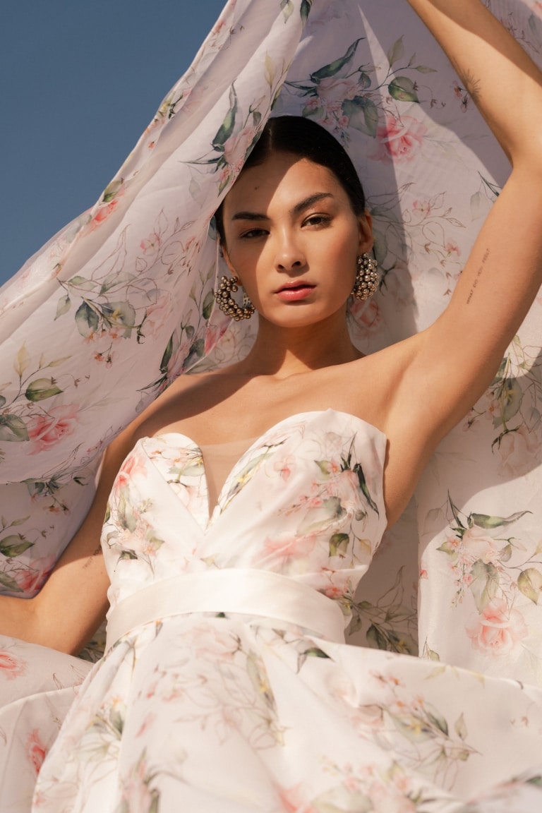 Woman in a pale floral dress raising a sheer veil above her head
