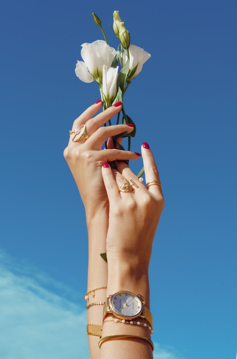 Hands with rings and a wristwatch holding a white flower