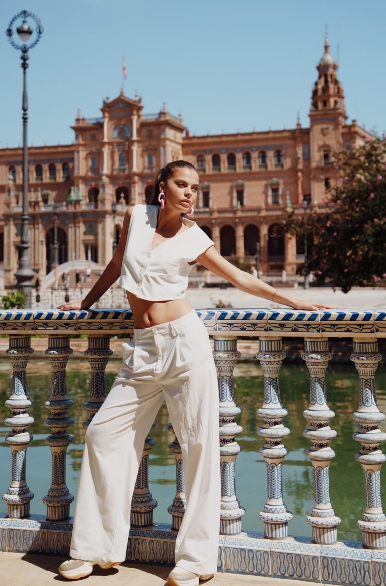 Woman in a white crop top and pale trousers beside an ornate tiled balustrade